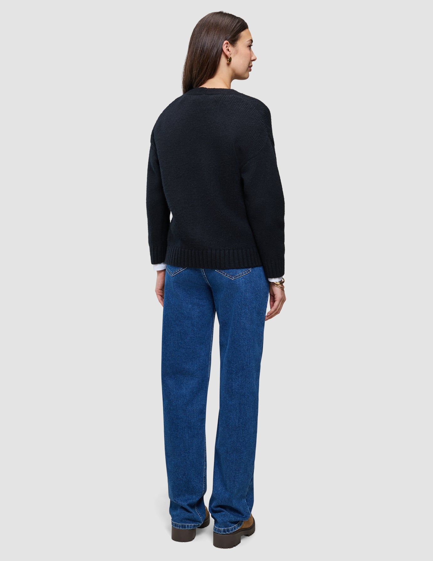 En person sedd bakifrån, klädd i en svart, tjock och mjuk stickad damkofta i ull över en vit skjorta och blå jeans.